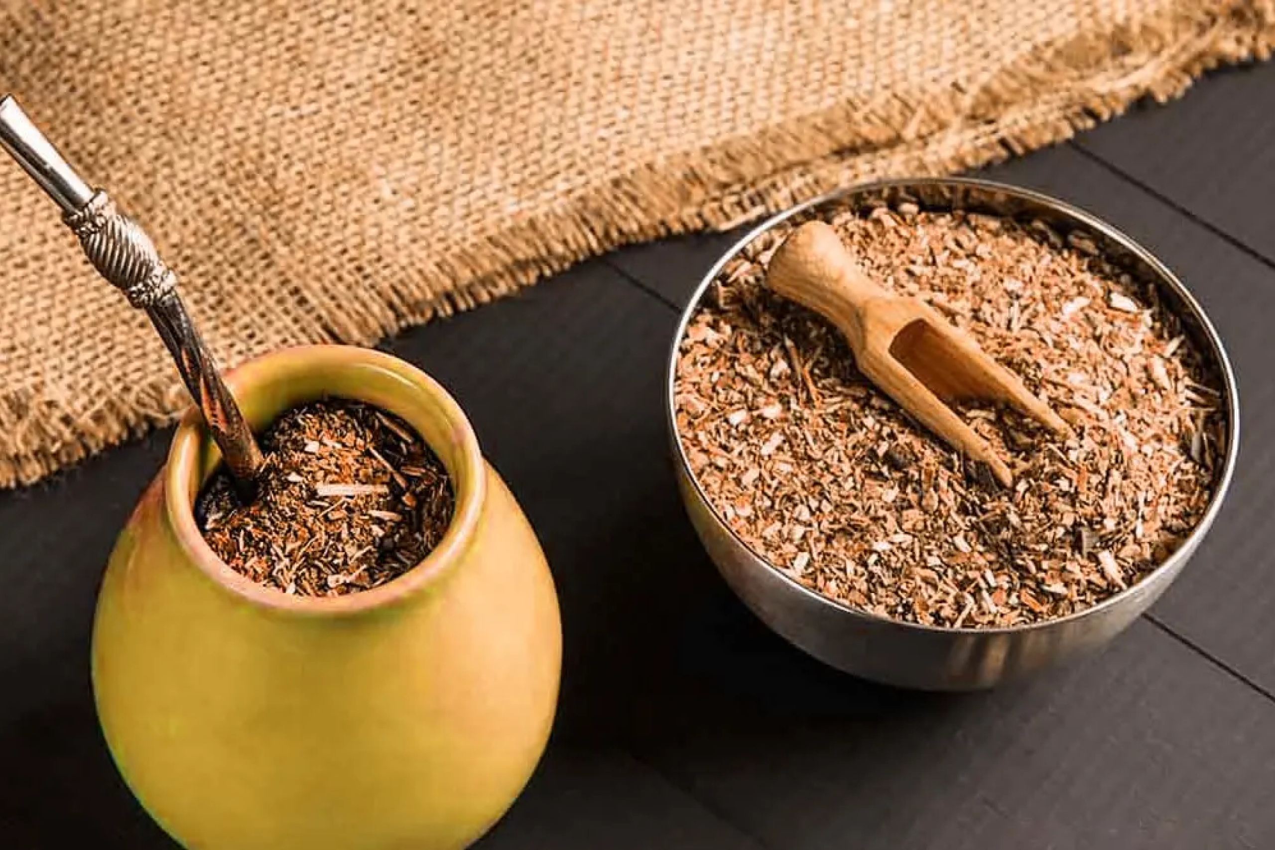 Yerba maté tea hagyományos mate csészében és bombillával tálalva, szárított yerba levelekkel körülvéve